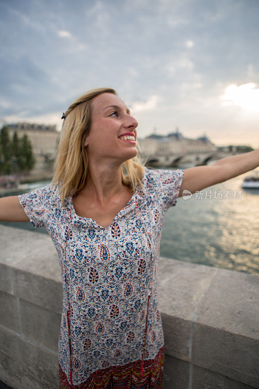 年轻快乐的女子站在俯瞰塞纳河的大桥上，双臂张开——自由