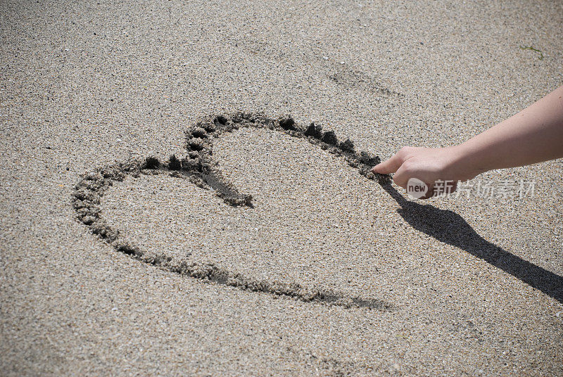 女人在沙滩上画心、画沙滩、画爱情的概念