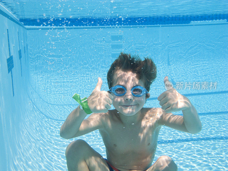 男孩在游泳池深处竖起大拇指。