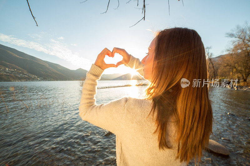 年轻女子在湖边做心形手指架