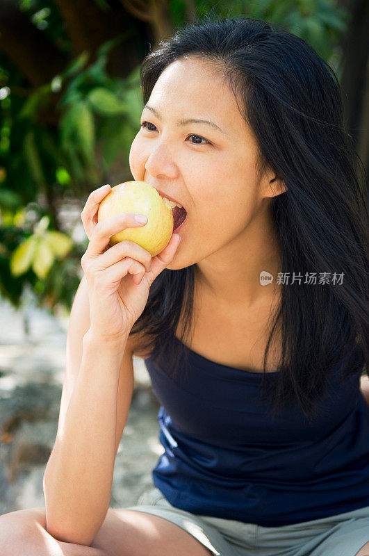 年轻的亚洲女子在户外吃咬苹果