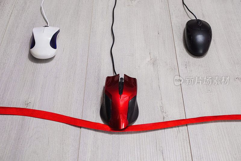 互动竞赛的速度之间的红色，白色和黑色的电脑鼠标在木制的背景。用于光标控制的输入设备。红丝带。商业竞争，繁文缛节。