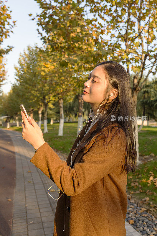 亚洲女人站在公园小径上听音乐