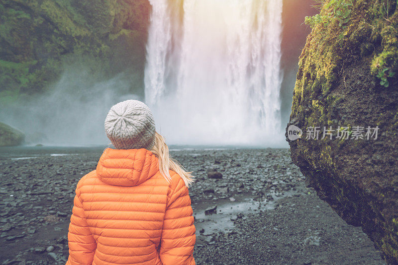 女游客在冰岛旅游时，站在壮丽的瀑布旁边，沉思大自然，人们旅行冒险的概念