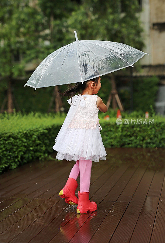 可爱的小女孩在雨中打着伞。