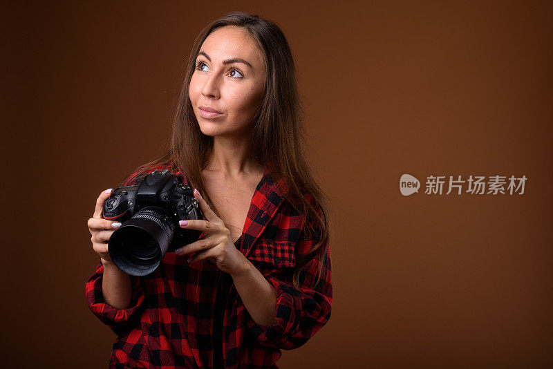工作室拍摄的年轻美丽的女人与相机穿着红色格子衬衫，以彩色背景