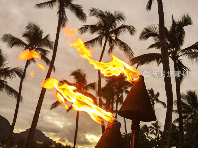 夏威夷海滩上点燃的提基火炬，以山为背景