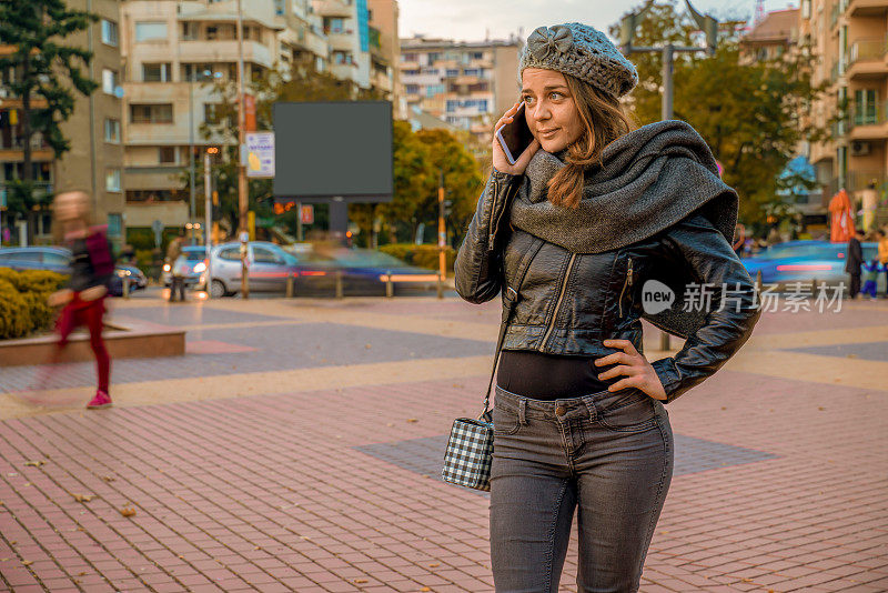 美丽的城市女孩讲她的智能手机在城市交通的背景