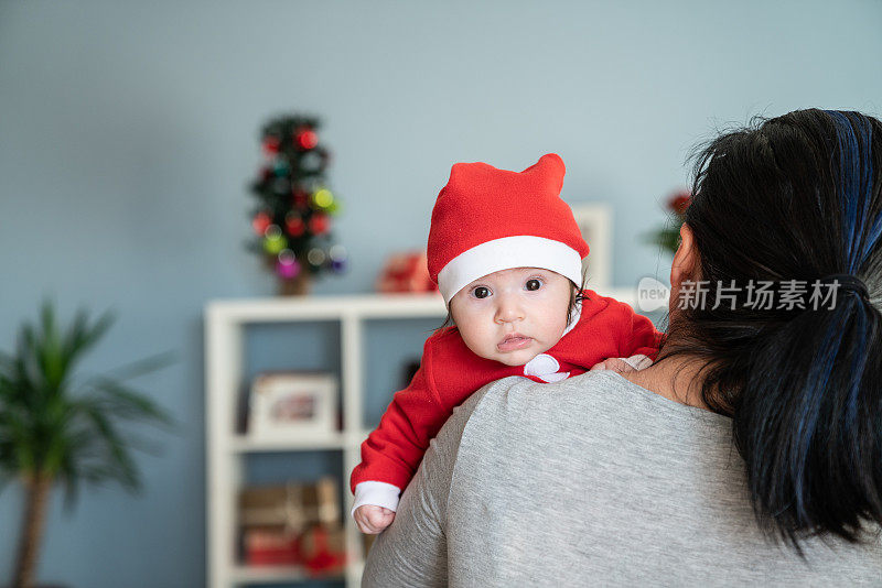 婴儿女孩的肖像在圣诞老人的服装凝视妈妈的肩膀