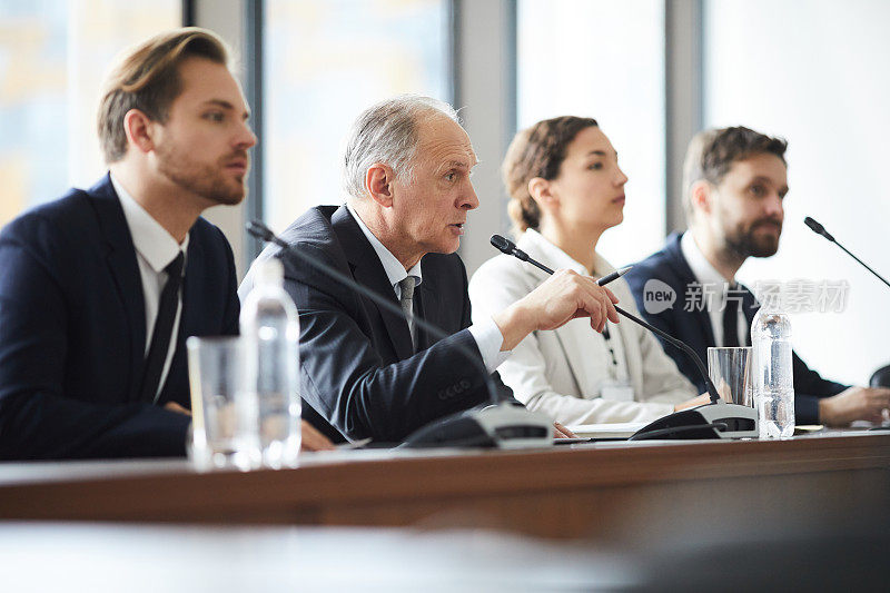 新闻发布会上的政客:严肃自信、头发花白的企业高管坐在一排同事中间，对着麦克风讲话，回答会议上的问题