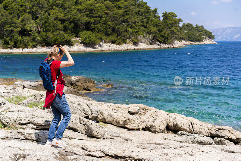 老妇人在克罗地亚Mljet岛附近的岩石上散步和吃三明治的侧面照片