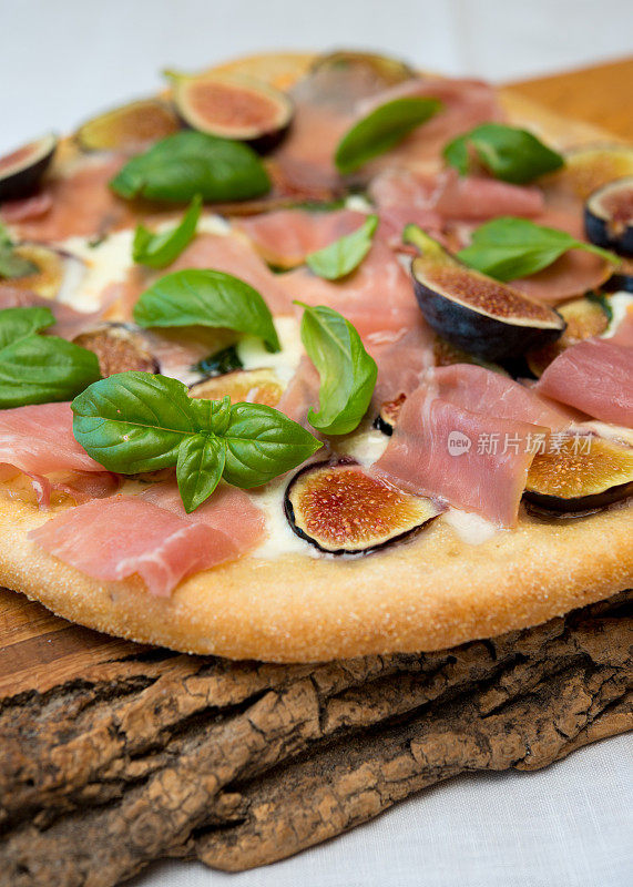 意大利熏火腿，新鲜无花果和水牛奶酪披萨放在乡村橡木砧板上