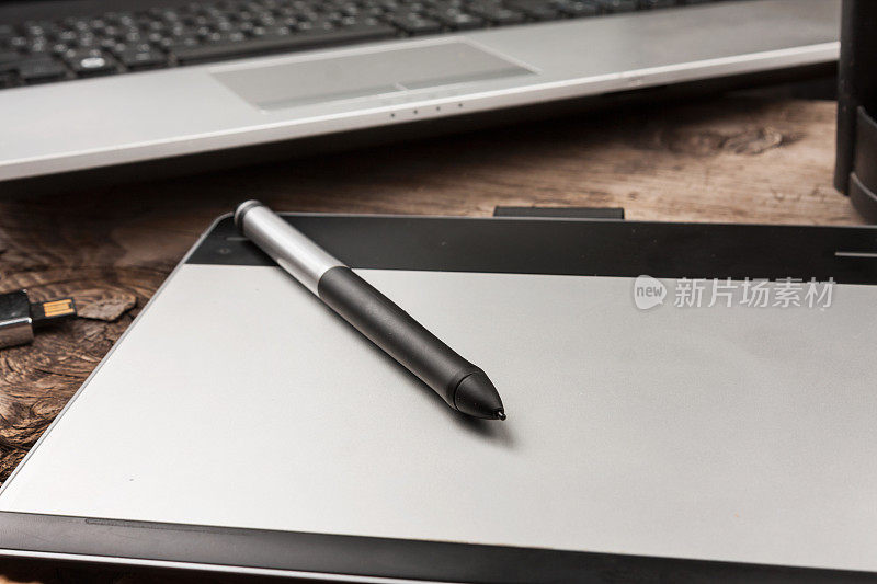 近距离拍摄的图形平板电脑与手写笔在一个笔记本电脑的背景。图形设计师必备工具。专业修图编辑设备。桌面