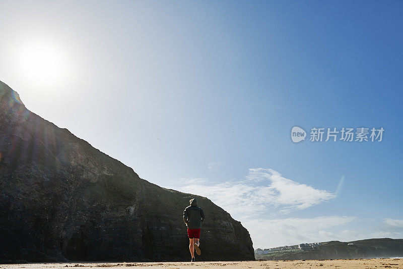 一个阳光明媚的秋日，康沃尔郡，沿着Perranporth海滩跑步的人。