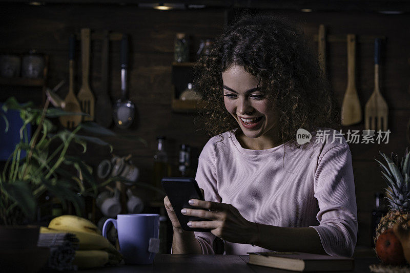 一个西班牙卷发的年轻女子在一个乡村厨房里用手机给一个朋友发短信