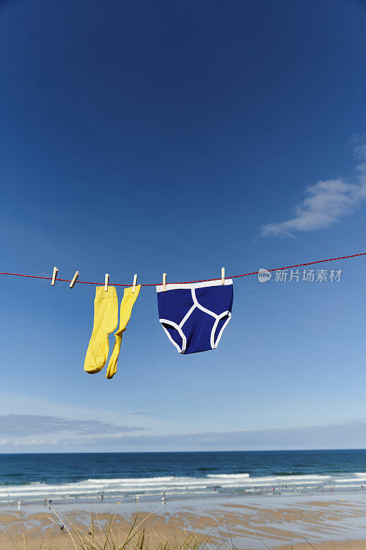 在阳光明媚的日子里，穿着黄色袜子和蓝色复古y型内裤的晾衣绳可以俯瞰海滩。