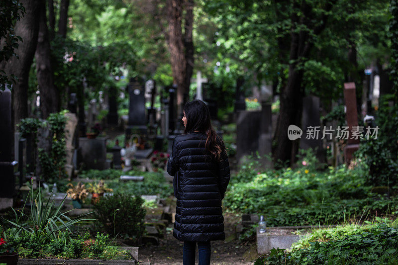 年轻女子走过老墓地与蓬松夹克在布拉格-绿色植物和树木