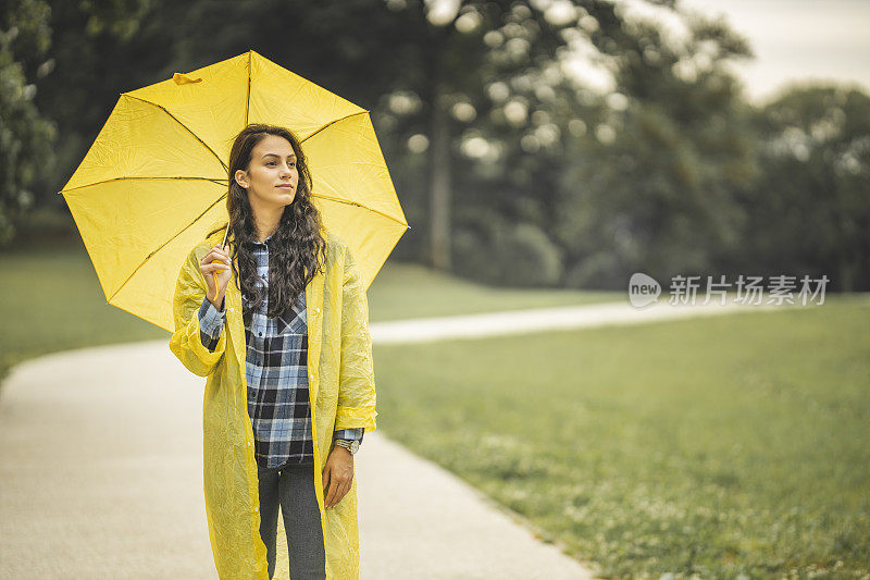 女人穿着雨衣，撑着雨伞，在雨天行走