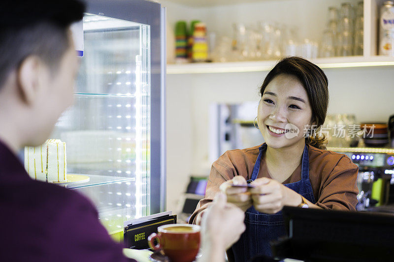 美丽的亚洲女招待收到信用卡无线支付客户在café。