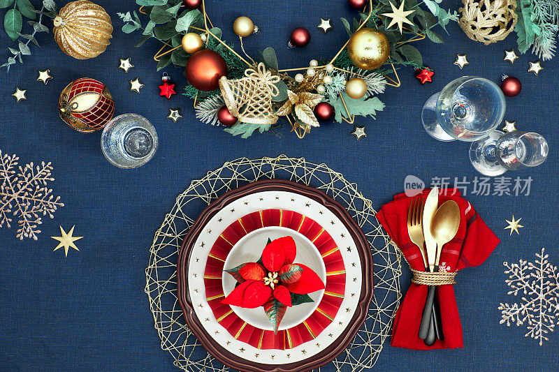 圣诞餐桌设置在金色，酒红色和经典的蓝色。平铺，俯视图装饰餐桌布局，金色的餐具，白色的星星盘子。传统的圣诞节装饰在经典的蓝色亚麻布上