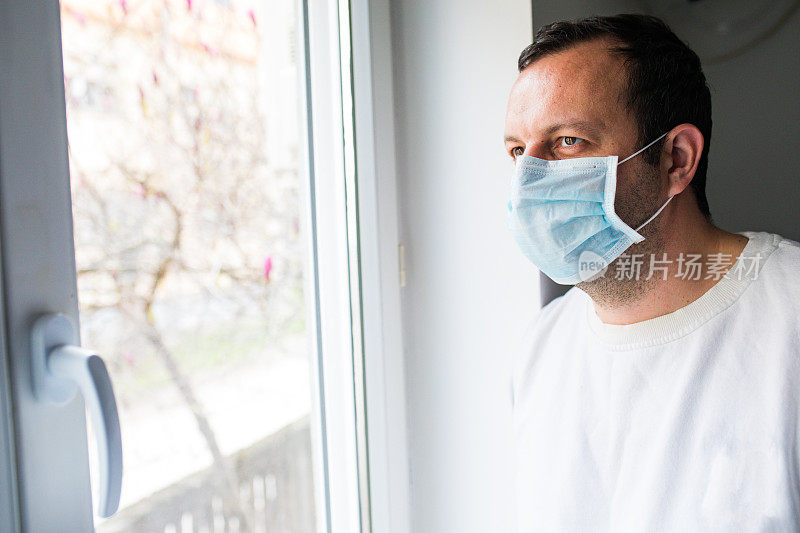 孤独的男人戴着医用口罩望着窗外。居家隔离自我隔离
