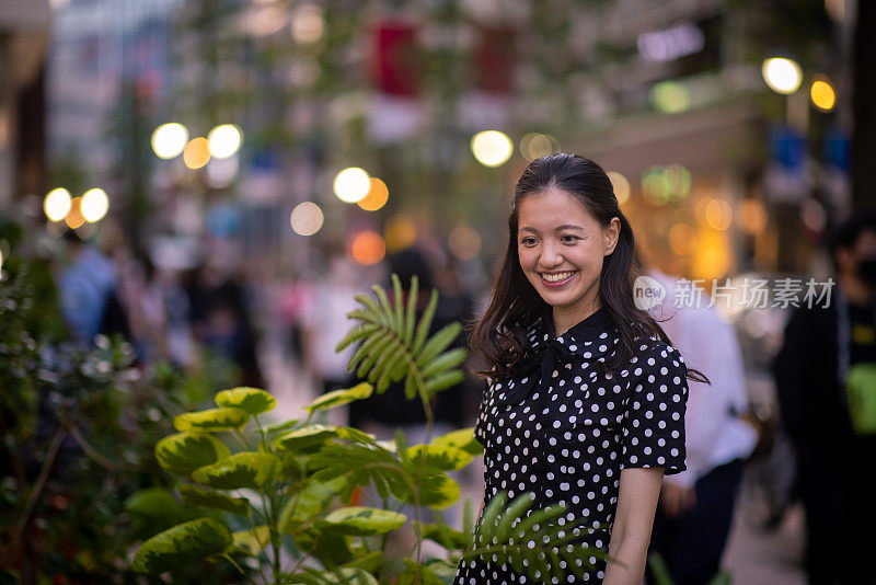 日落时分，年轻女子站在城市街道的花店前