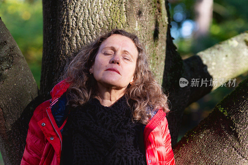 成熟的女人在秋天的户外，倚着树，闭着眼睛