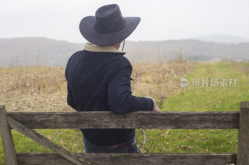 成年男性农民，靠在他农场的木篱笆上