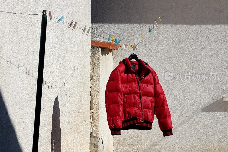 刚洗过的大红冬季夹克挂在衣架上晾干，晾在挂满晒衣夹的晾衣绳上