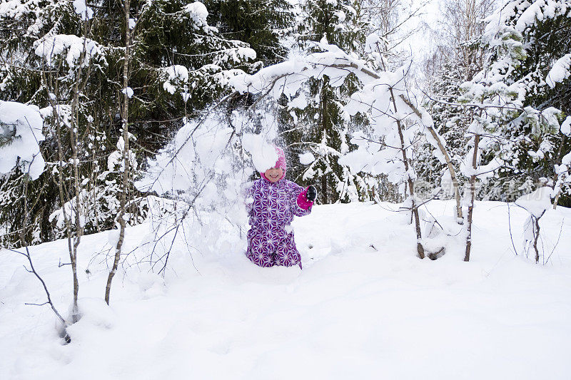 一个孩子，一个5岁的白种人女孩，身上洒满了雪。女孩在冬天的森林里玩得很开心。