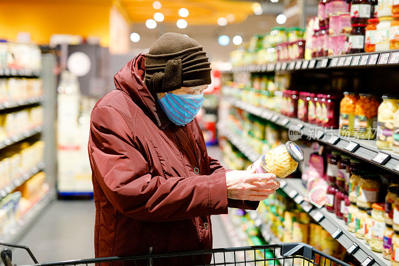 老年妇女戴医用口罩，防范大流行性冠状病毒病。90岁退休女性推购物车在超市购物。女人买食物和杂货