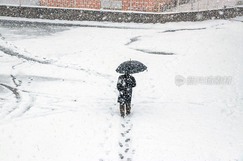 一个男人在大雪中撑着伞走