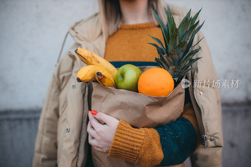 一个年轻的女人拿着一个装着新鲜水果的纸袋