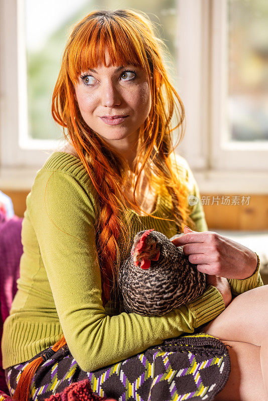 坐在窗边，一个年轻漂亮的女人住在一个农场里，抱着一只小鸡当宠物。