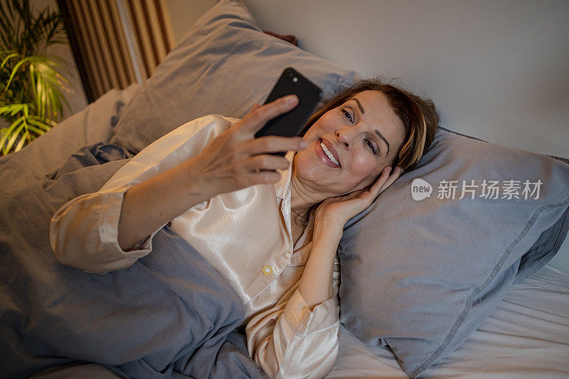 成熟的女人晚上躺在床上看智能手机