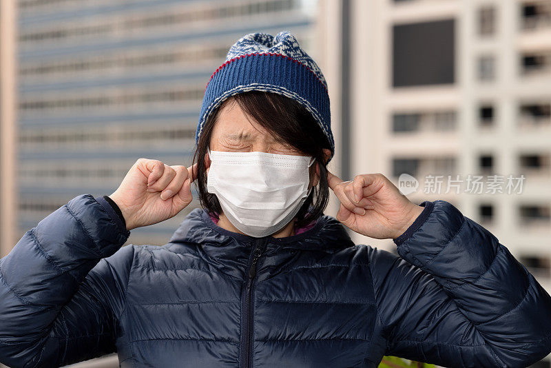 戴着口罩用手指捂住耳朵的女人