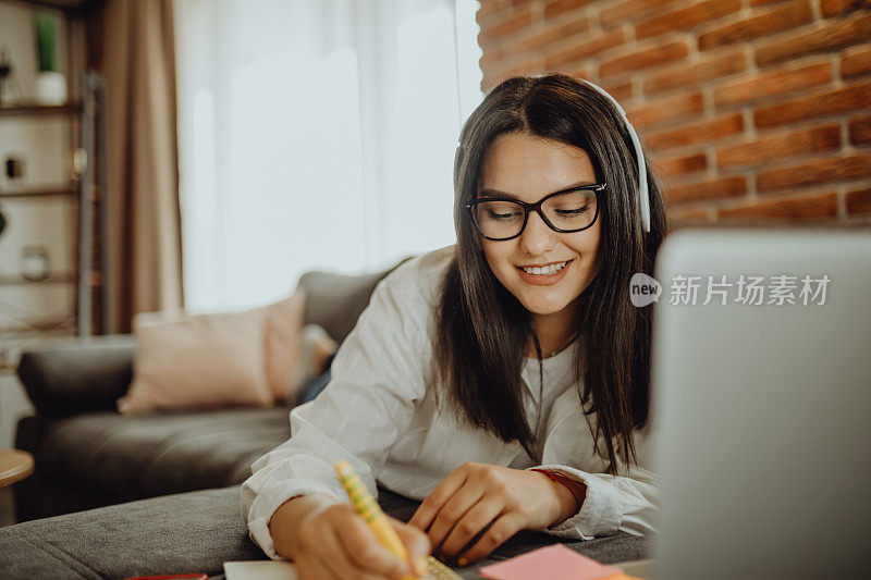 一位年轻的女学生坐在沙发上使用笔记本电脑耳机学习