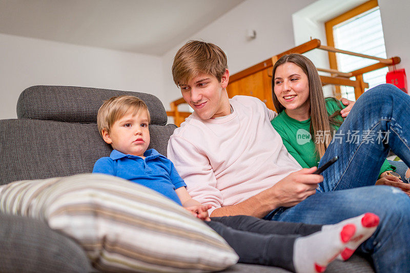 年轻的一家人坐在沙发上看电视