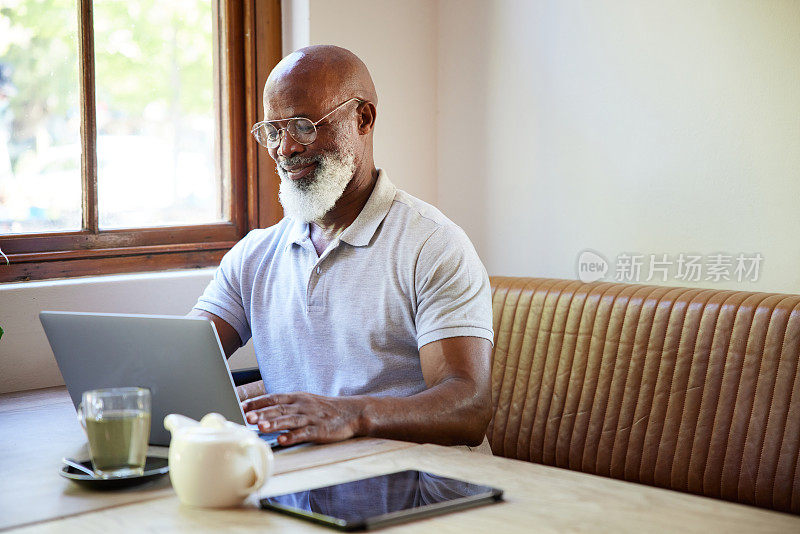 一个微笑的成熟男人在咖啡馆里用笔记本电脑工作