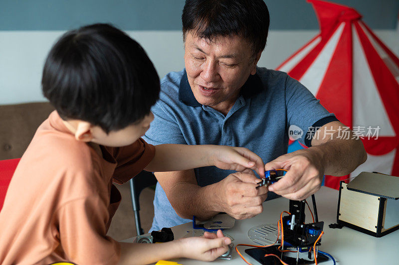 亚洲男孩在家里和爷爷一起制作机器人玩具