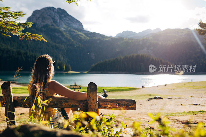 从一个无法辨认的女人的背后看到的风景，她坐在湖边的长椅上享受大自然。