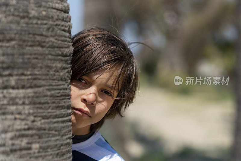 害羞悲伤的男孩从树后看着