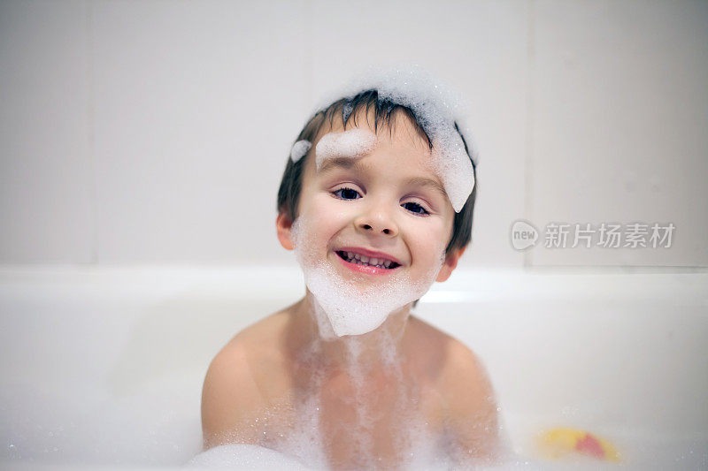 可爱的男孩在浴缸晚上的时间，微笑着，覆盖着肥皂泡沫