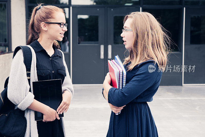 两个青少年在高中门口聊天。