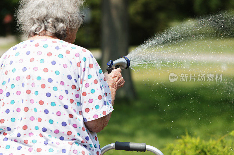 年长妇女用花园软管喷水