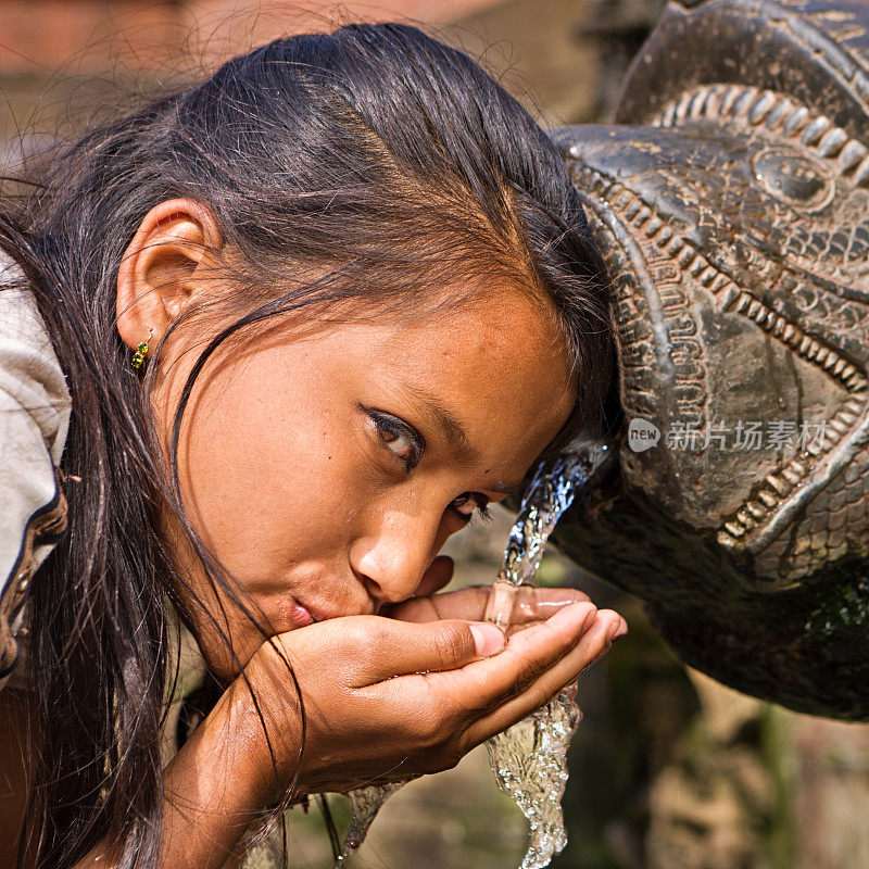 年轻的尼泊尔女孩在杜巴广场的城市喷泉中饮水