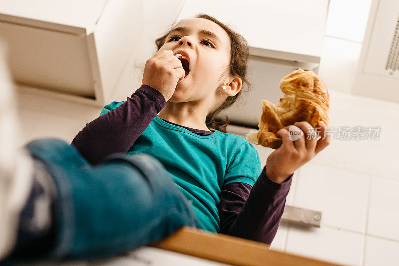 可爱的小女孩在厨房吃牛角面包