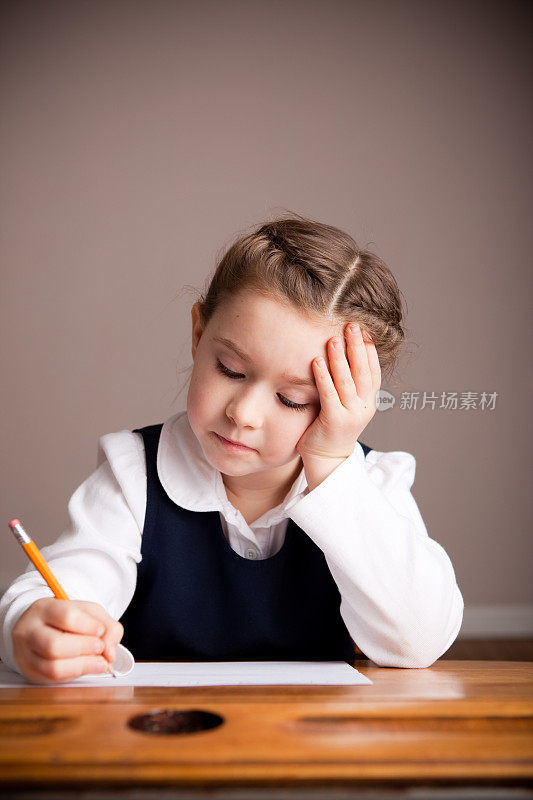年轻的女学生坐在学校书桌上写作