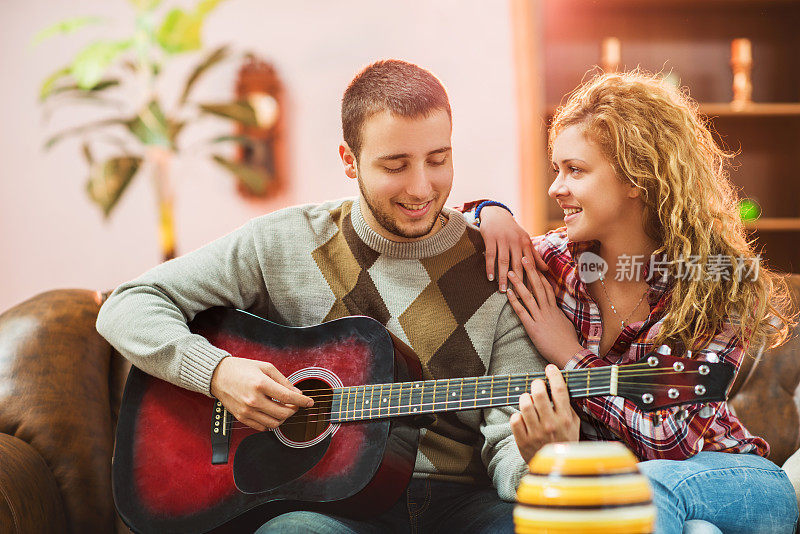 微笑的男人给他的女朋友弹吉他。