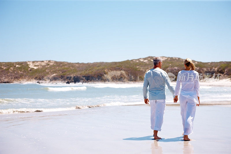 后视图:一对情侣在海滩上散步时手牵着手